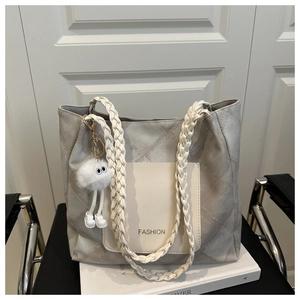 Detail of grey quilted tote bag with woven handles and fashion logo on front pocket