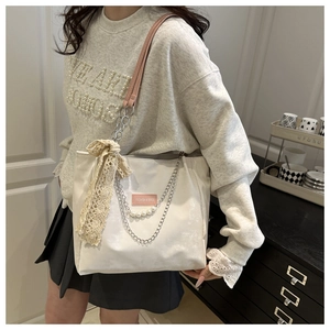 Close-up of white tote bag with pink straps, silver chain, pearls and lace bow detail