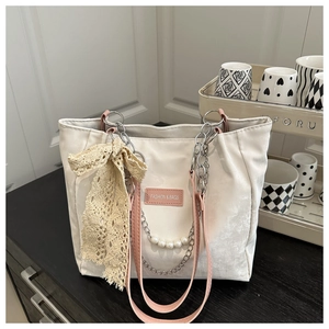 Détail du cabas blanc avec nœud en dentelle beige, perles et lanières en cuir rose