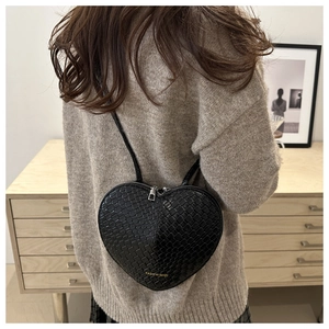 Detail of black heart-shaped crossbody bag with woven texture and gold fashion logo