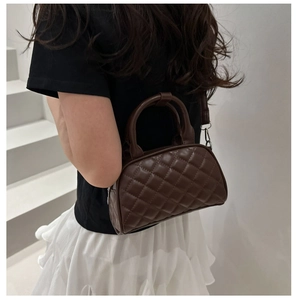 Close-up of quilted dark brown boston bag with metal hooks and cross-body strap detail