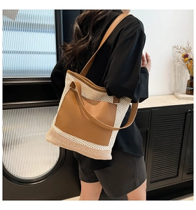 Detailed shoulder view of a large beige straw tote bag with brown leather front pocket