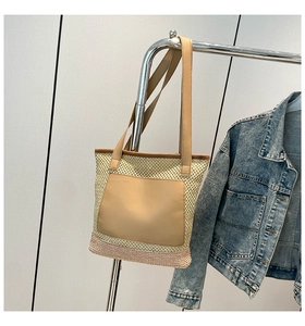 Detailed close-up of woven straw tote bag with leather pocket and shoulder strap