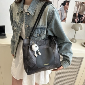 Black woven texture tote bag with leather pocket and plush monster charm on shoulder strap
