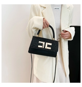 Detail showing elegant black handbag with gold geometric buckle and leather strap