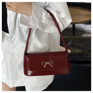 Détail du sac baguette rouge foncé avec boucle en nœud doré et bandoulière en cuir souple