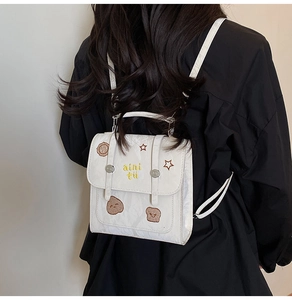 Detail of white backpack featuring yellow aini tu embroidery and star patches on model