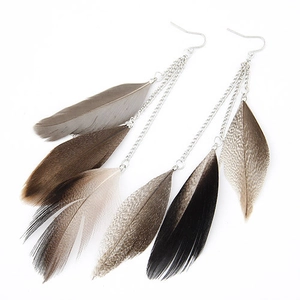 Macro detail of bohemian long tassel earrings with natural feathers and delicate metal chains
