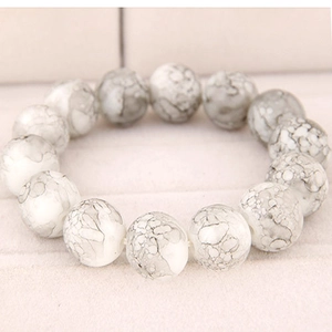 Macro shot of white marble textured round beads on a minimalist jewelry display cushion