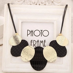 Détail d'un grand collier bohème avec pendentifs martelés dorés et textures noires