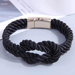 Braided black PU leather bracelet with gold magnetic metal clasp on a textured surface