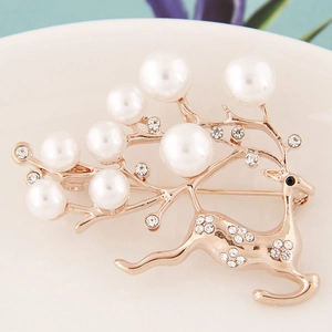 Elegant gold reindeer brooch with white pearls and sparkling crystals on a white ceramic plate