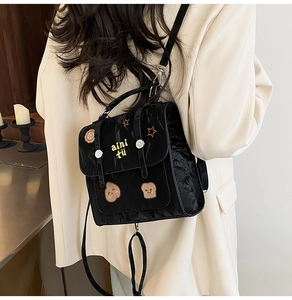 Detail of black pleated crossbody bag with yellow embroidery and star patches on a model