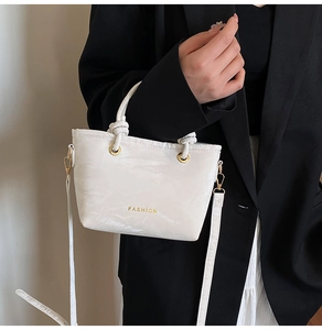 Close-up of white pleated bucket bag with gold 'FASHION' lettering and metal hardware
