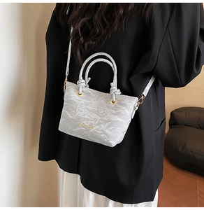Close-up of a light grey pleated bucket bag with gold Fashion text and metallic strap