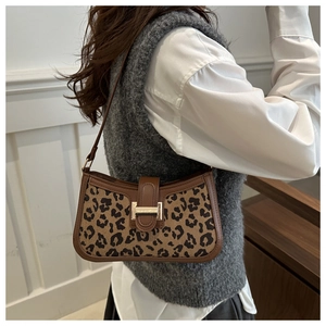 Détail du sac léopard sous le bras avec bordure en cuir marron et fermoir doré