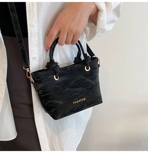 Close-up of black bucket bag featuring crinkled texture, gold rings and Fashion logo