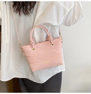 Detail of light pink pleated bucket bag with knotted handle and golden fashion lettering