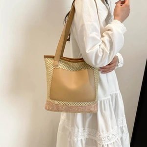 Large beige woven straw tote bag with brown leather pocket shown on model shoulder