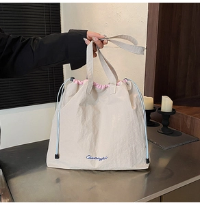 Gros plan sur le sac fourre-tout en nylon crème avec broderie bleue et doublure rose