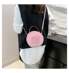 Pink round crossbody bag with SM embossed logo shown on a textured stone background