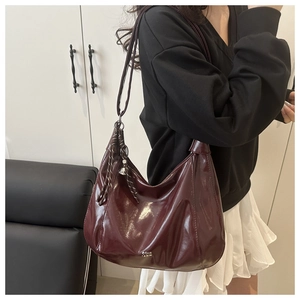 Close-up of wine red hobo bag in glossy patent leather with silver charm and tassels