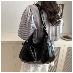 Detail of glossy black leather hobo bag with tassel and logo shown on a shoulder