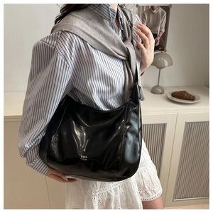 Close-up of black glossy oversized hobo bag with silver logo detail and leather texture
