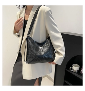 Close-up of black woven shoulder bag with silver butterfly emblem on a white blazer