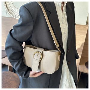 Détail du sac sous l'aisselle beige avec boucle dorée vintage sur une veste grise chic