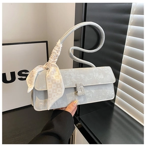 Détail d'un sac baguette argenté avec boucle en strass et poignée ornée d'un foulard