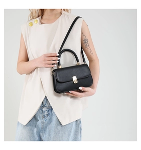 Detail of a black leather crossbody bag with a gold metal twist lock on a beige vest model