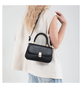 Side view of a black square crossbody bag with gold buckle on a model wearing jeans
