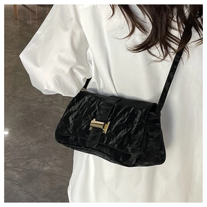 Detail of black pleated baguette bag with gold metal clasp on white oversized shirt