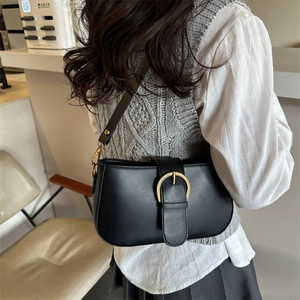 Sac sous le bras noir minimaliste avec boucle dorée porté par un mannequin au café