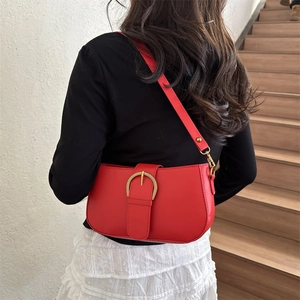 Sac sous le bras rouge avec boucle dorée porté par un mannequin dans un style épuré