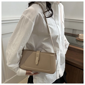 Model wearing a khaki rectangular shoulder bag with golden cylinder clasp and long strap