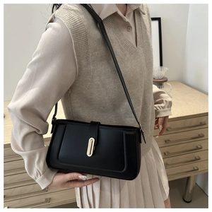 Close-up of minimalist black leather shoulder bag with golden oval buckle and slim strap