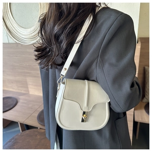 Detailed back-view of cream saddle bag on model wearing grey suit in a warm interior