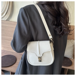 Detailed view of a white saddle bag with golden clasp worn over a grey blazer jacket
