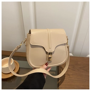 Detailed view of the gold-tone metal twist lock on a cream saddle bag with leather strap