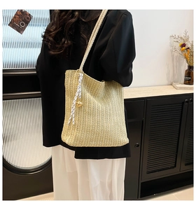 Detail of woven straw tote bag featuring rope handles and decorative ribbon on model