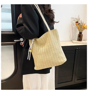 Detail of woven straw tote bag featuring thick rope handles and striped ribbon ornament
