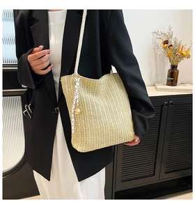 Detail of handwoven beige straw tote bag with gold bell and striped ribbon charm
