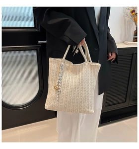 Detail of beige straw woven tote bag featuring natural texture and decorative tassel charm