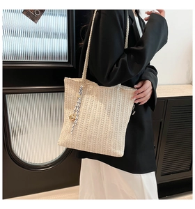 Détail d'un sac cabas tissé beige avec ruban à rayures bleues et pendentif doré