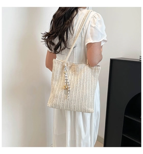 Detail view of cream woven tote bag texture and decorative cord tassel on a model