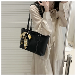 Detail of a black leather tote bag featuring contrast white stitching and floral silk scarf
