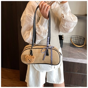 Detail of hand-woven straw shoulder bag with bear pendant and blue checkered ribbon