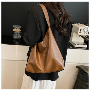 Brown large tote bag in textured leather shown over the shoulder in a cafe setting